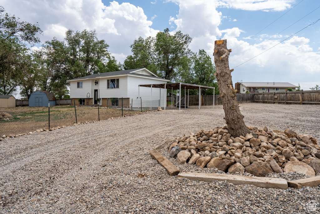 Back of house featuring gravel driveway, a storage shed, a fenced backyard, and a carport