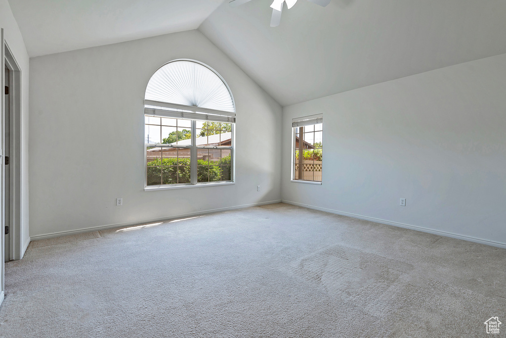 Carpeted empty room featuring vaulted ceiling and a ceiling fan