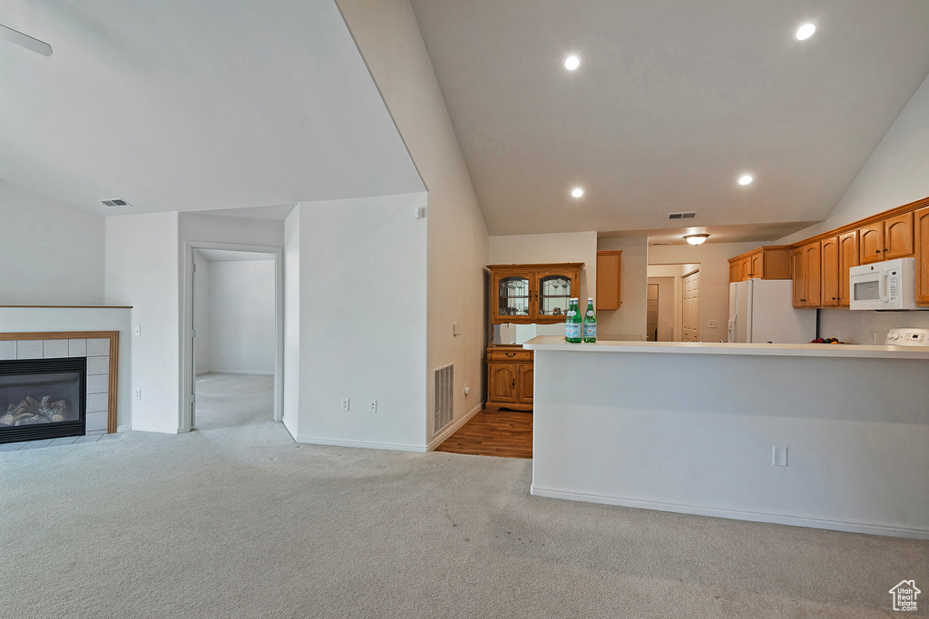 Kitchen featuring light carpet, open floor plan, vaulted ceiling, white appliances, and recessed lighting
