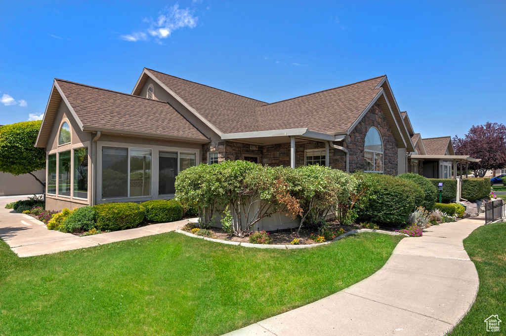 Back of property with stone siding, a lawn, and roof with shingles