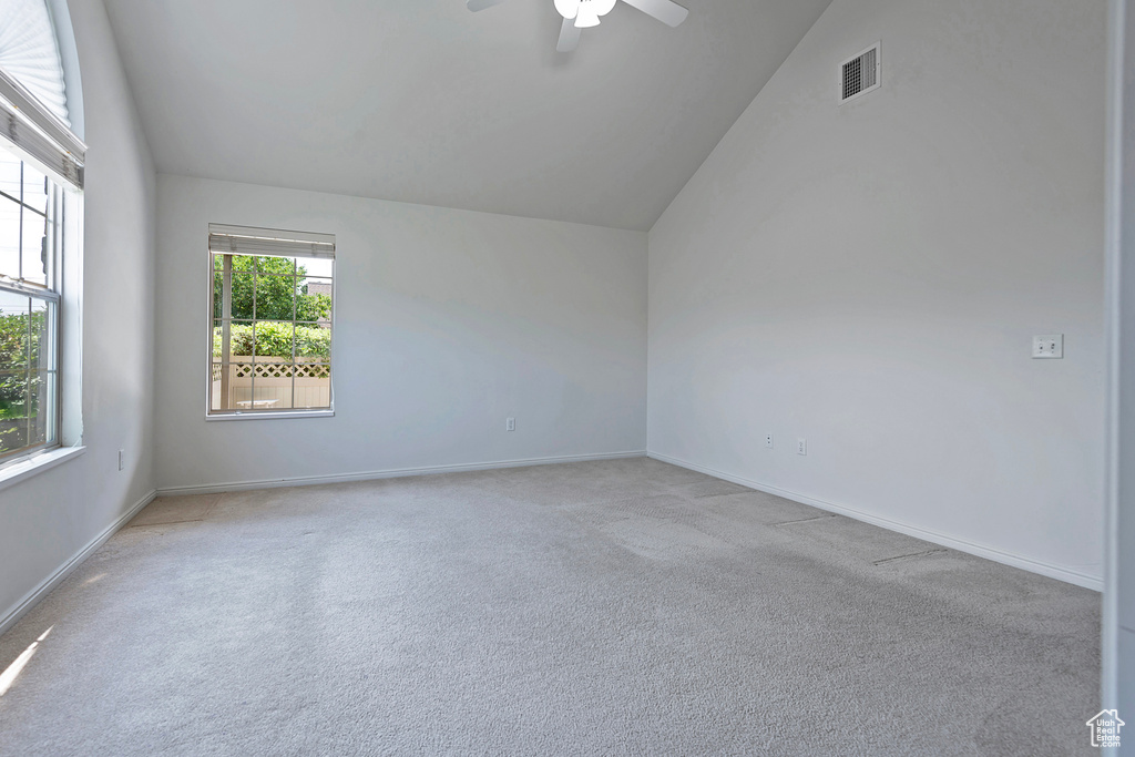 Empty room featuring vaulted ceiling, light carpet, and a ceiling fan