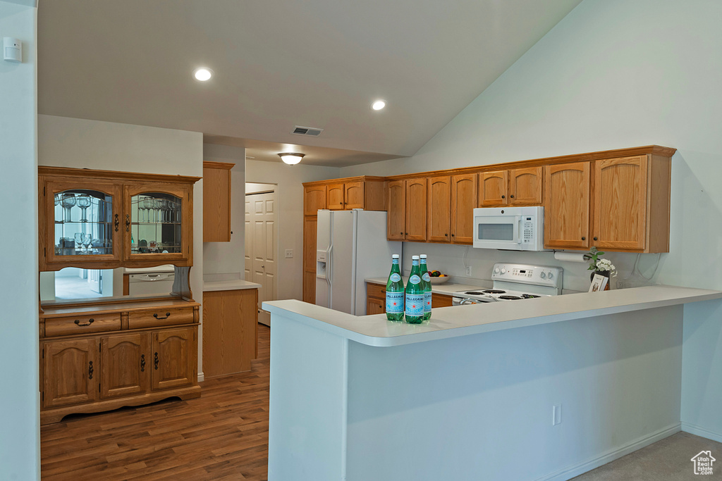 Kitchen with light countertops, white appliances, a peninsula, recessed lighting, and wood finished floors