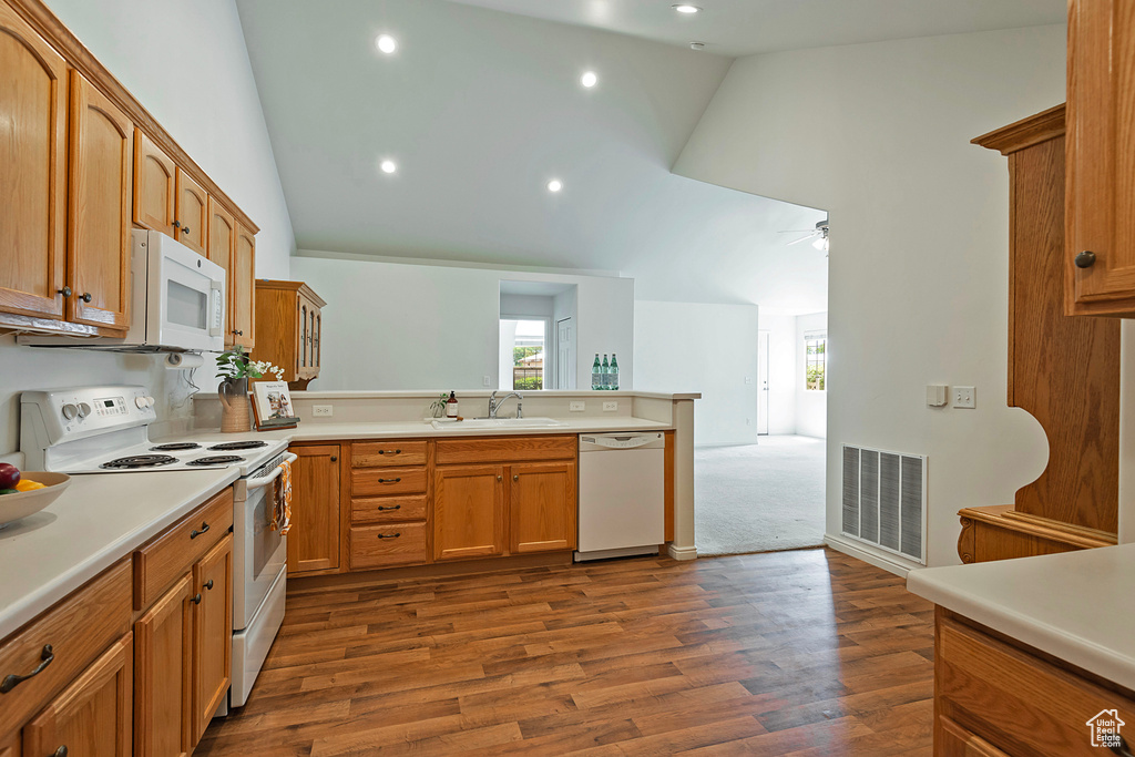 Kitchen featuring white appliances, a peninsula, high vaulted ceiling, plenty of natural light, and light countertops