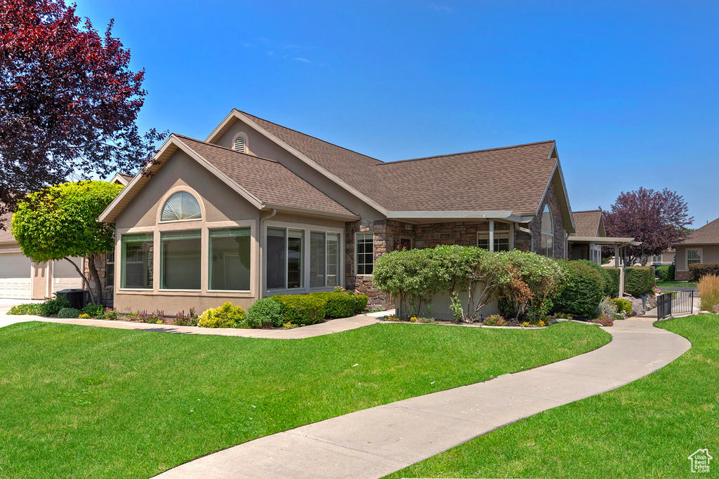 View of side of home featuring stone siding, a lawn, roof with shingles, and stucco siding