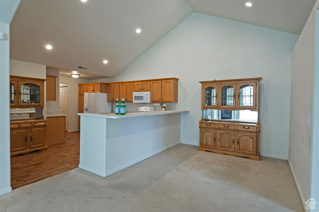 Kitchen with light carpet, a peninsula, light countertops, white appliances, and high vaulted ceiling