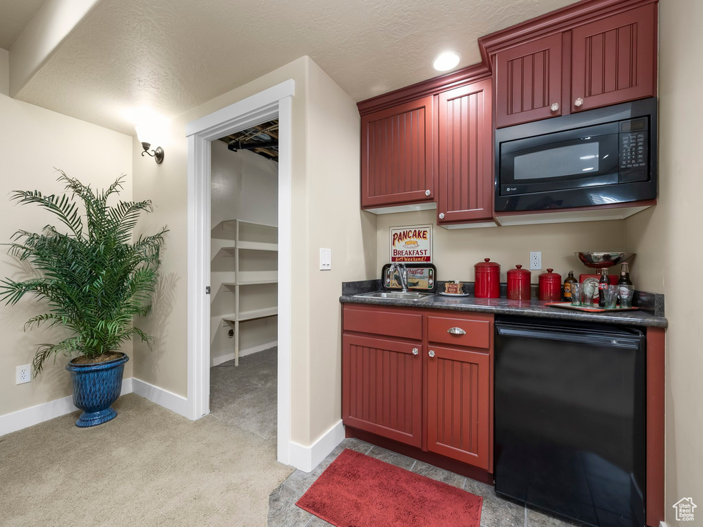 Kitchen with black microwave, reddish brown cabinets, dark countertops, and light colored carpet
