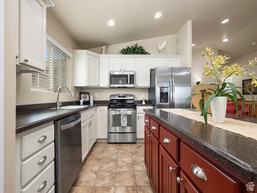 Kitchen with appliances with stainless steel finishes, vaulted ceiling, white cabinetry, and recessed lighting