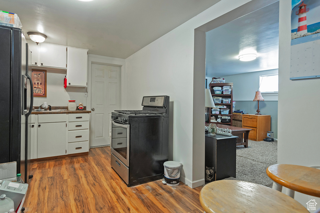 Kitchen with stainless steel gas range, black fridge with ice dispenser, wood finished floors, and white cabinets