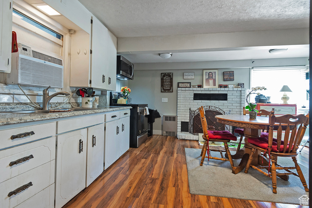 Kitchen with appliances with stainless steel finishes, dark wood finished floors, a fireplace, white cabinetry, and light countertops