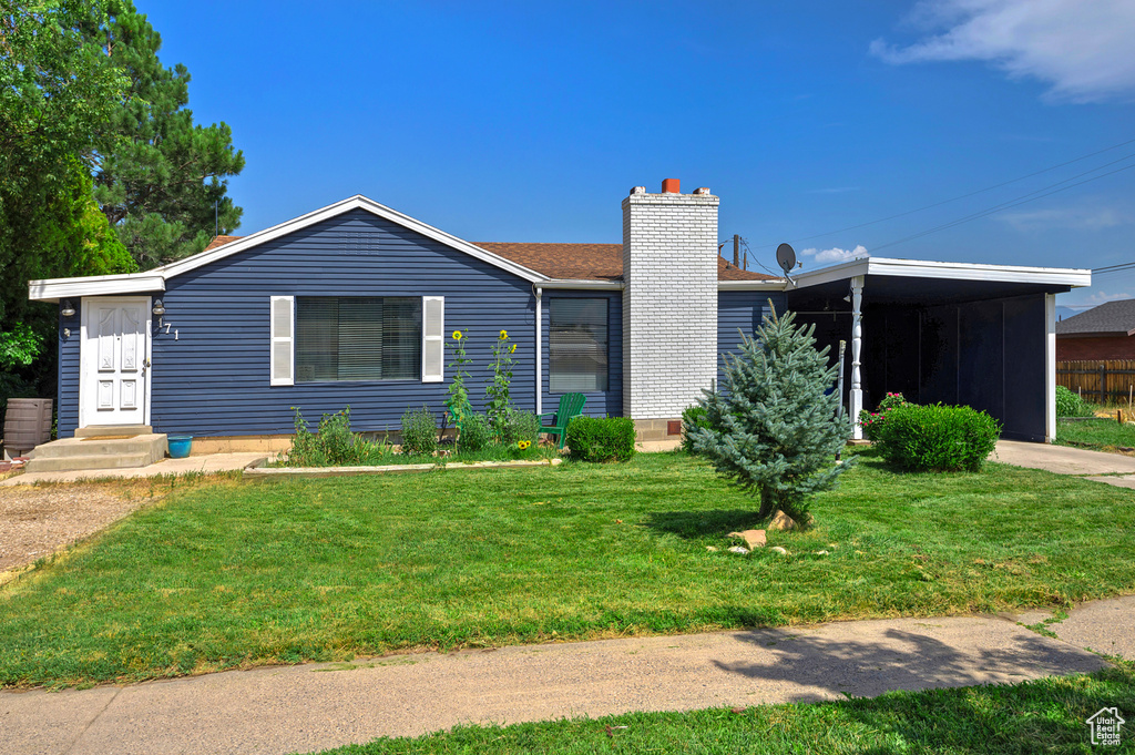 View of front of property with a chimney, a front yard, and an attached carport