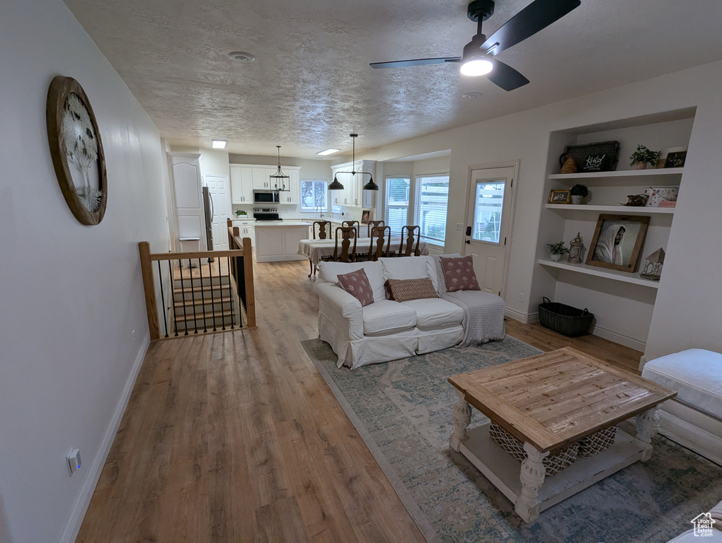 Living area featuring light wood-style flooring, a ceiling fan, a textured ceiling, and built in features