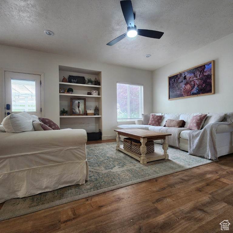 Living room with a textured ceiling, wood finished floors, built in shelves, and ceiling fan