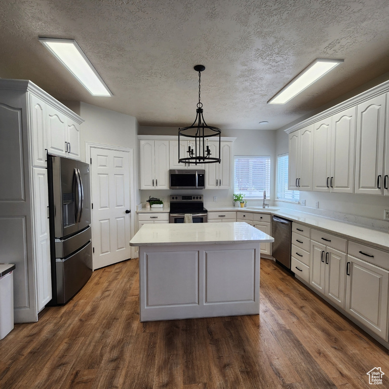 Kitchen with appliances with stainless steel finishes, a center island, white cabinets, light countertops, and dark wood-style floors