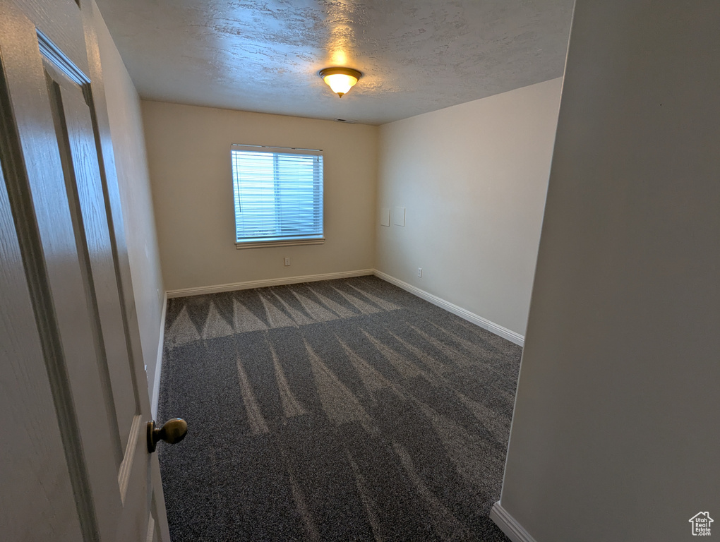 Unfurnished room featuring a textured ceiling and dark colored carpet