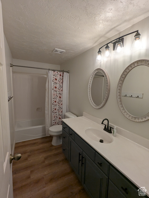 Full bath with a textured ceiling, wood finished floors, vanity, and shower / bathtub combination with curtain