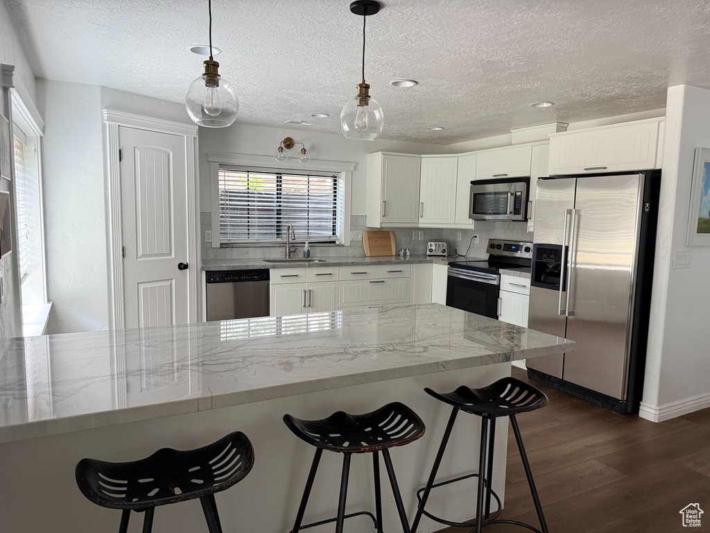 Kitchen with appliances with stainless steel finishes, a textured ceiling, dark wood finished floors, a kitchen bar, and white cabinetry