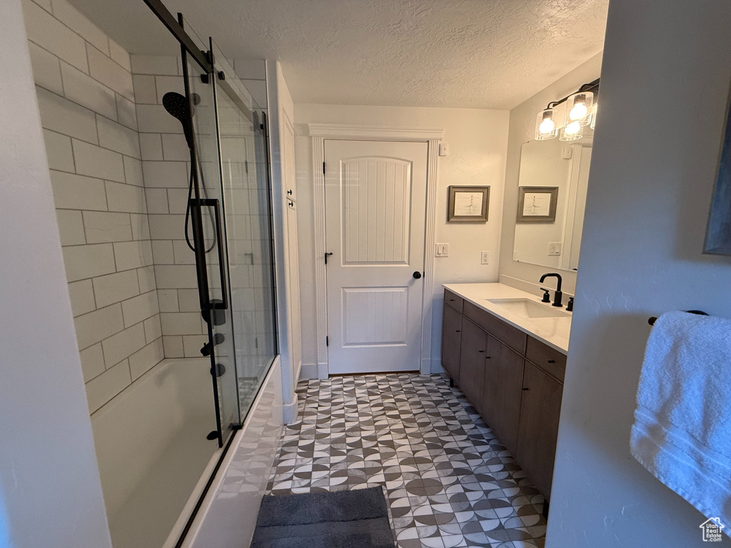 Full bath with enclosed tub / shower combo, vanity, a textured ceiling, and tile patterned floors