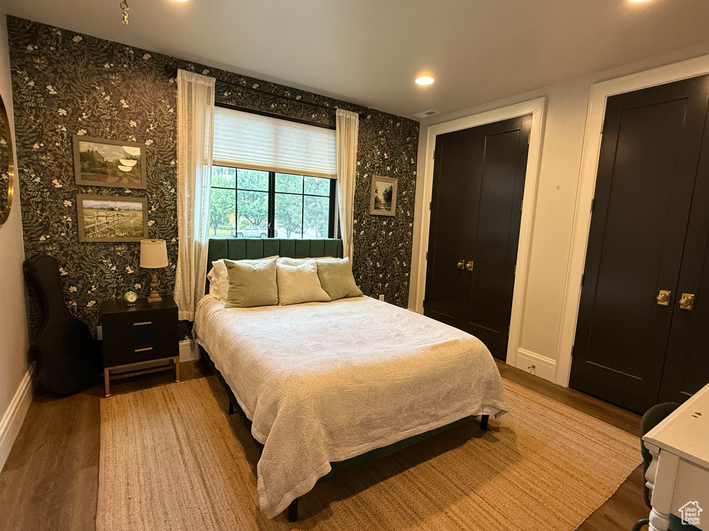Bedroom with wood finished floors, wallpapered walls, recessed lighting, and a closet