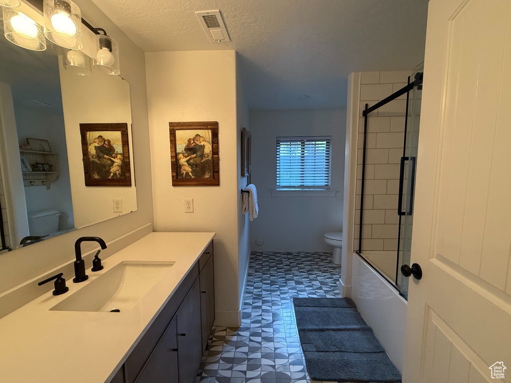 Full bathroom with tile patterned floors, vanity, combined bath / shower with glass door, and a textured ceiling