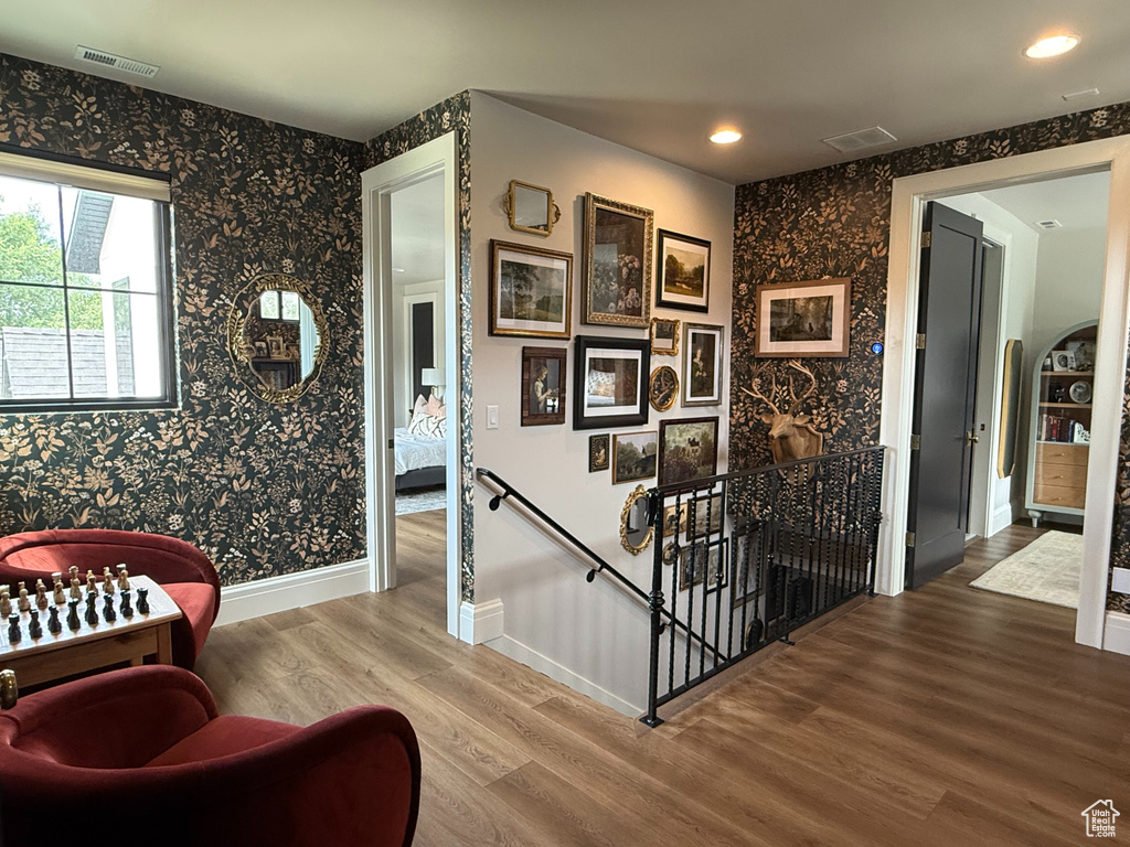 Corridor with an upstairs landing, wallpapered walls, wood finished floors, and recessed lighting
