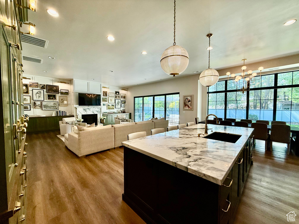 Kitchen featuring dark wood finished floors, a kitchen island with sink, a chandelier, recessed lighting, and light stone counters
