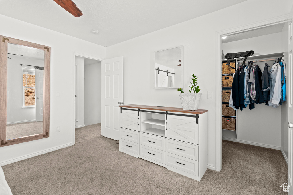 Bedroom with a spacious closet, light colored carpet, and ceiling fan