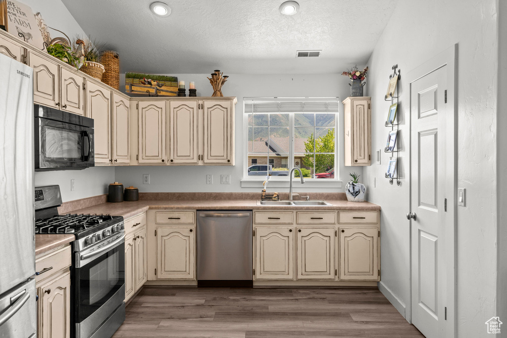 Kitchen with cream cabinetry, stainless steel appliances, light wood-type flooring, a textured ceiling, and light countertops