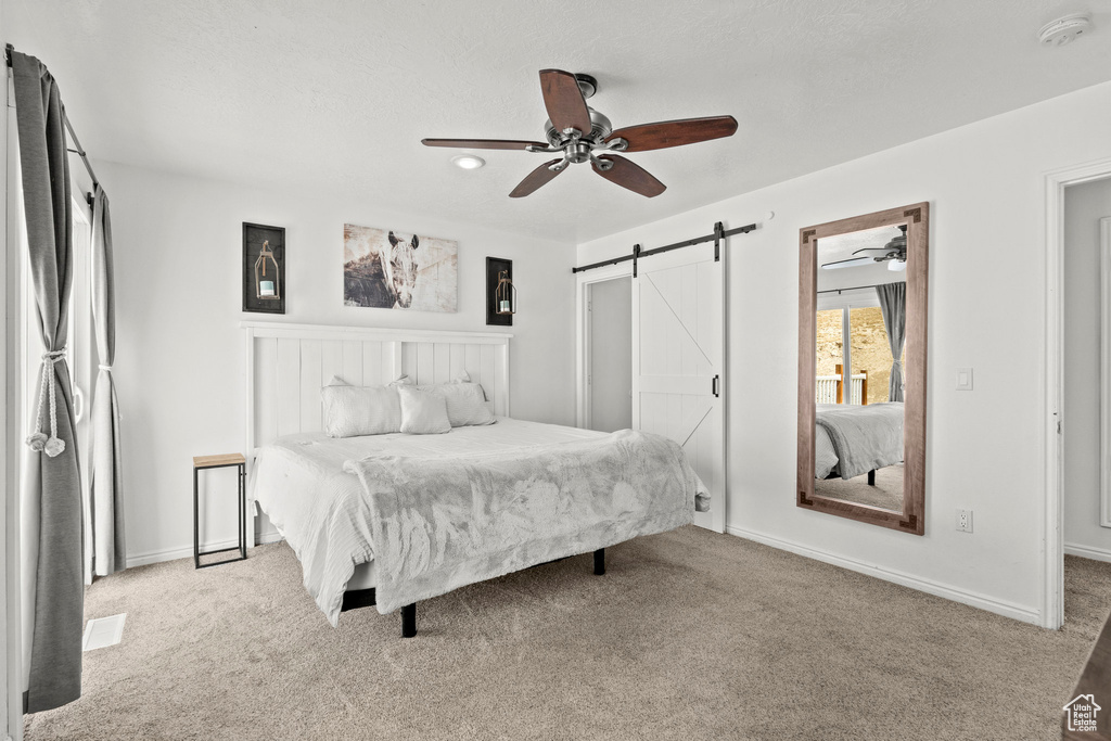 Carpeted bedroom featuring a barn door and a ceiling fan