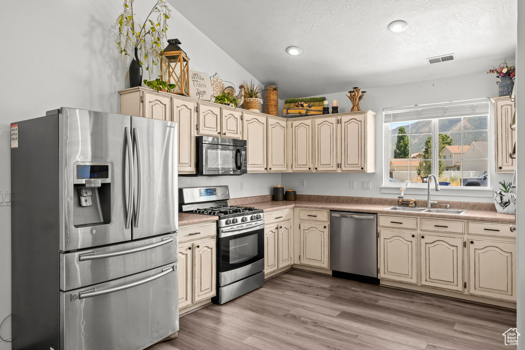Kitchen with appliances with stainless steel finishes, cream cabinets, a textured ceiling, light wood-style flooring, and light countertops