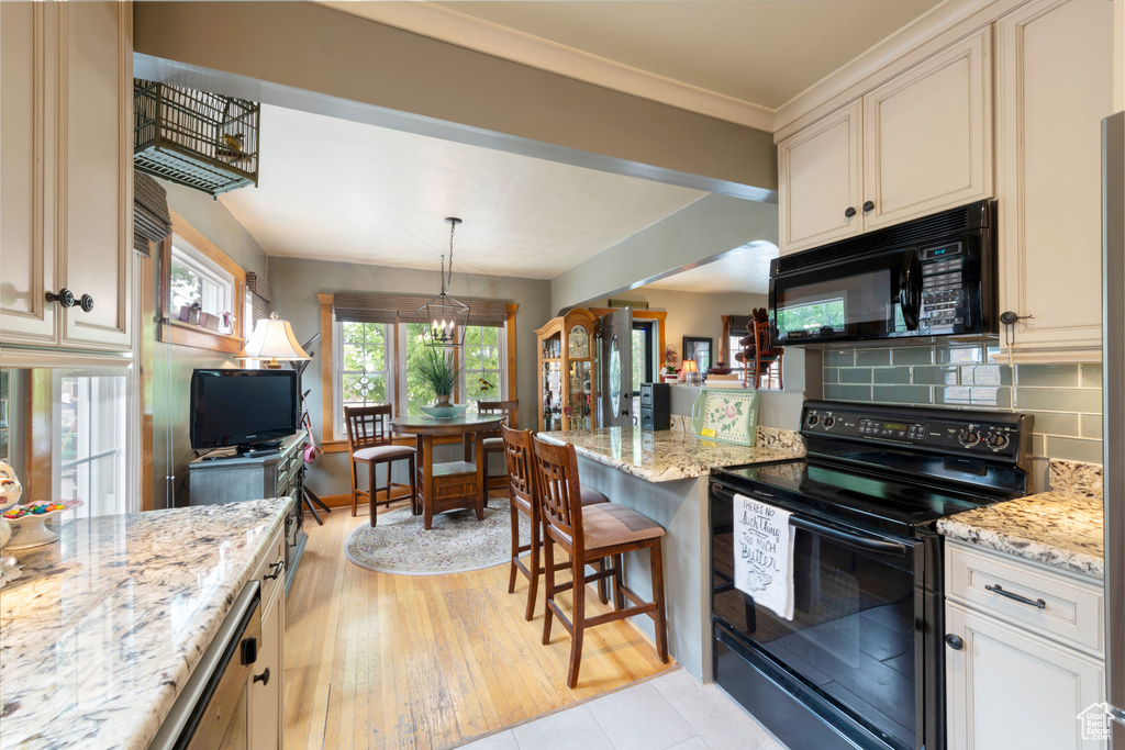 Kitchen with black appliances, backsplash, light stone countertops, and decorative light fixtures
