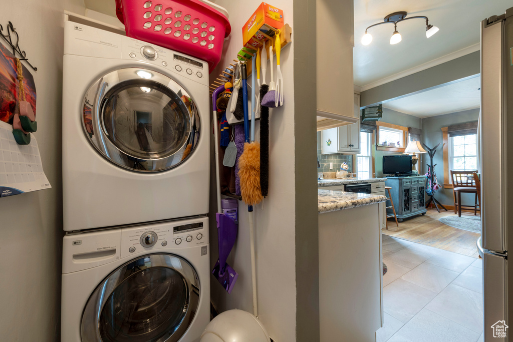 Laundry room featuring stacked washer / dryer, crown molding, and light tile patterned flooring