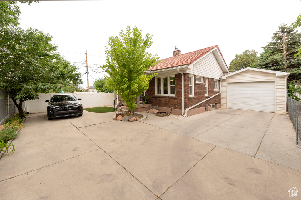 View of front of home featuring a garage, brick siding, driveway, an outdoor structure, and a chimney