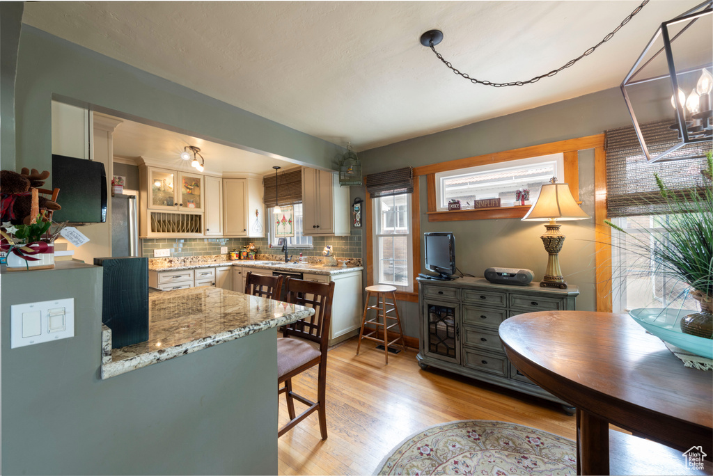 Kitchen with light wood finished floors, decorative backsplash, a kitchen breakfast bar, light stone counters, and glass insert cabinets