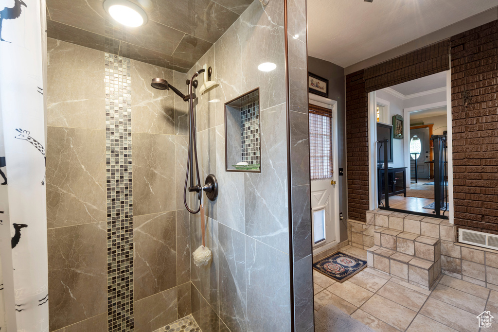 Full bath featuring tiled shower, crown molding, and tile patterned flooring