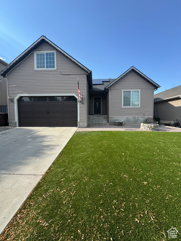 View of front of home featuring solar panels, driveway, a front lawn, and an attached garage