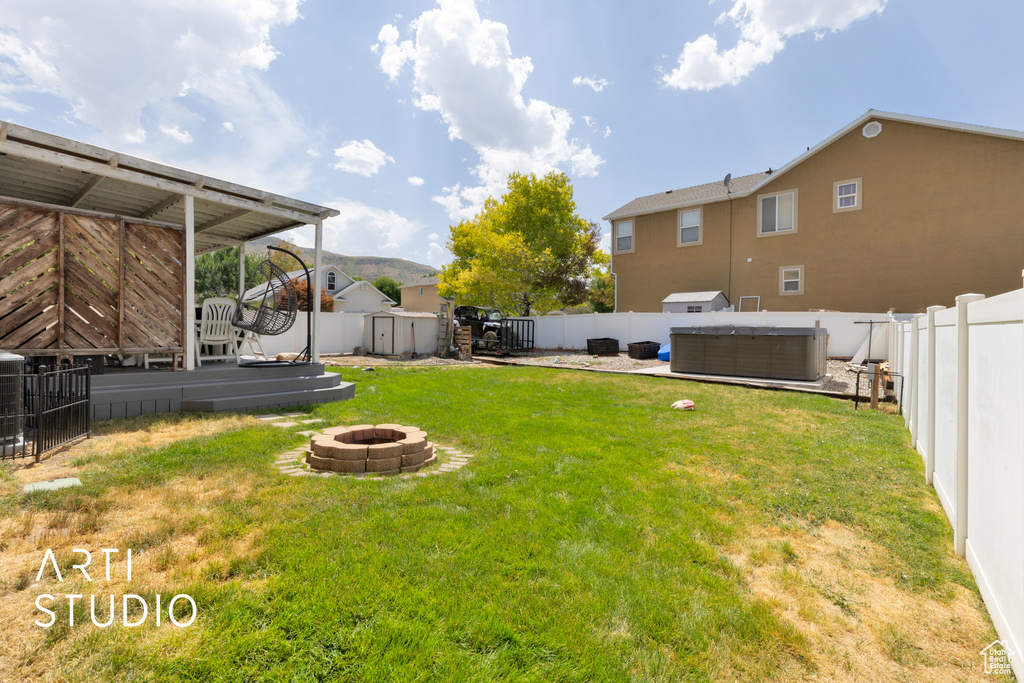 Fenced backyard with a fire pit, a storage shed, and a hot tub