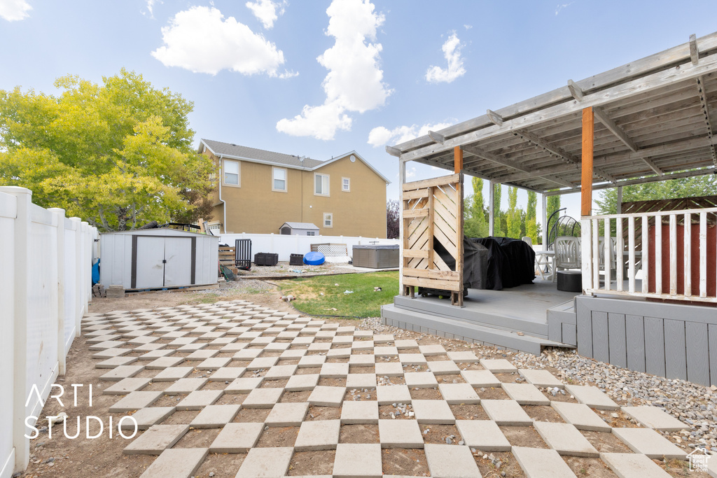 Fenced backyard with a storage unit, a patio area, a wooden deck, a grill, and a hot tub