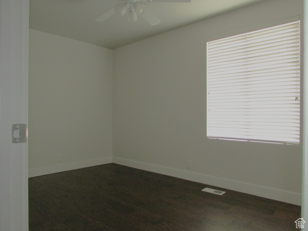 Spare room with a ceiling fan, plenty of natural light, and dark wood-type flooring