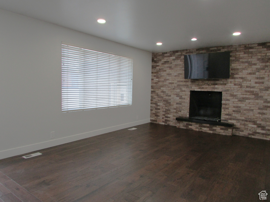 Unfurnished living room featuring dark wood-type flooring, a brick fireplace, and recessed lighting