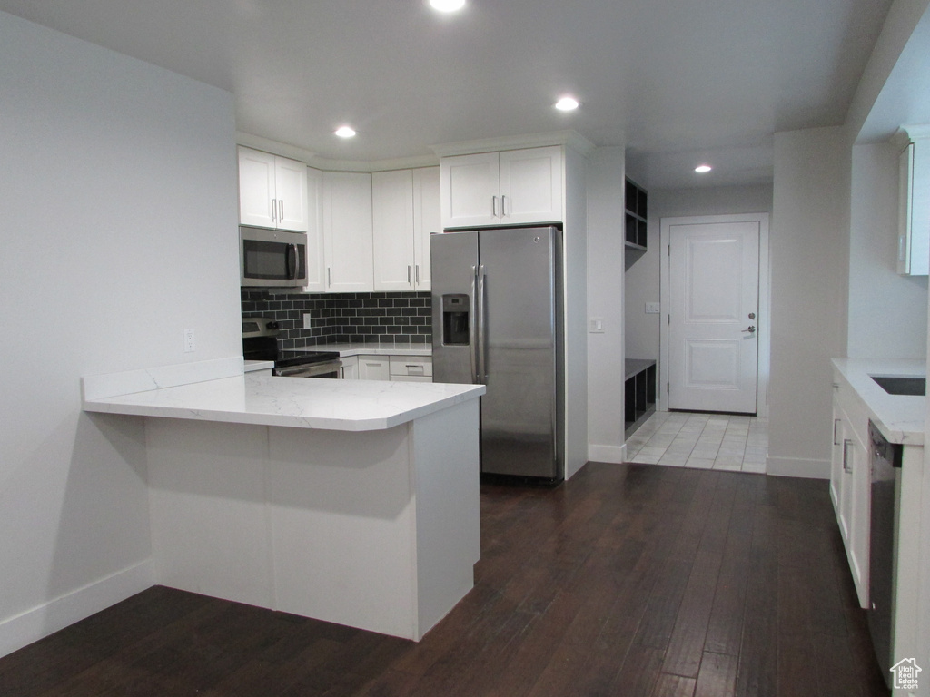 Kitchen with stainless steel appliances, a peninsula, white cabinets, light stone countertops, and tasteful backsplash