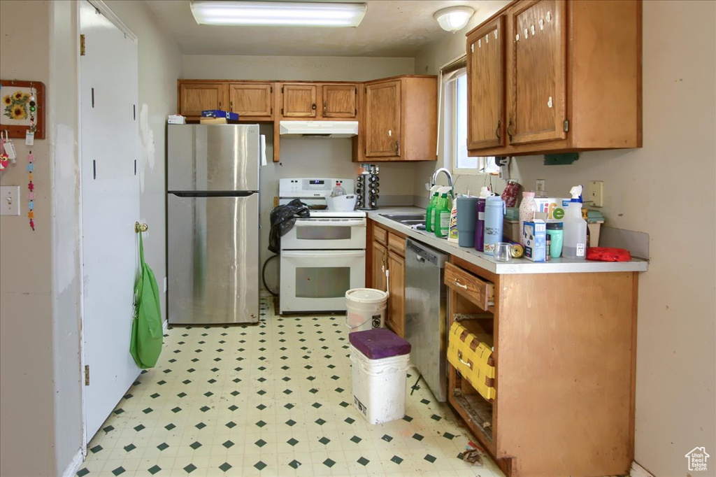 Kitchen featuring appliances with stainless steel finishes, light flooring, light countertops, brown cabinetry, and under cabinet range hood