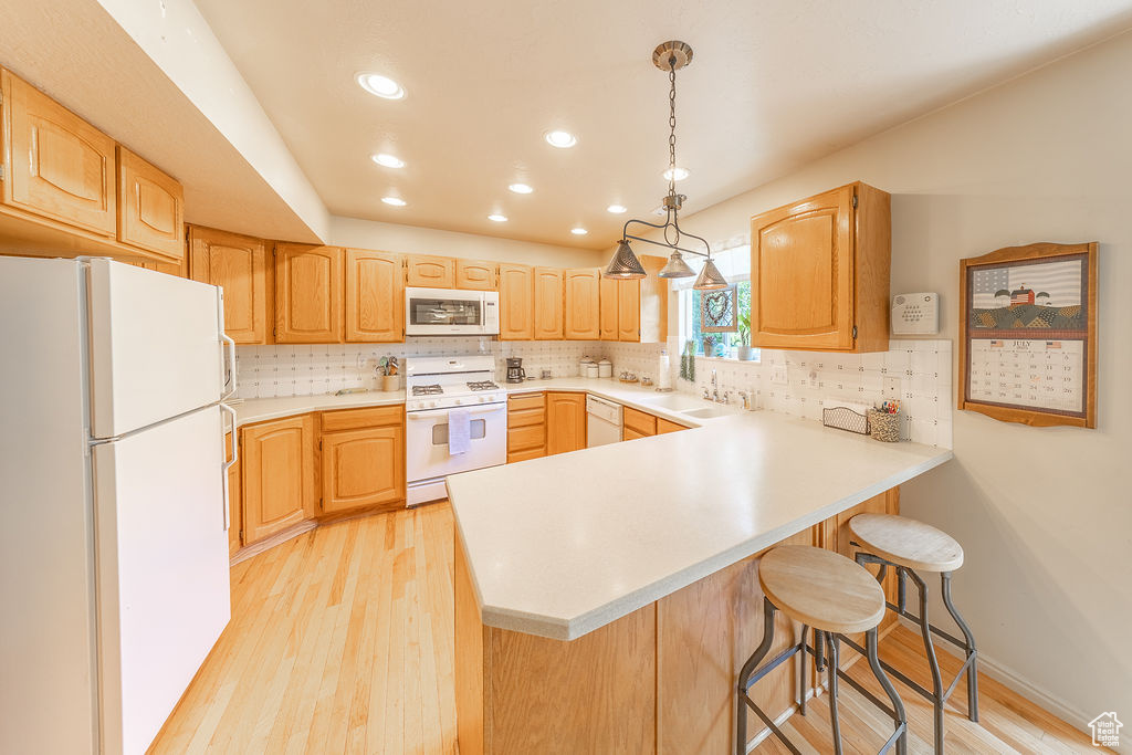 Kitchen featuring white appliances, a peninsula, light wood finished floors, tasteful backsplash, and recessed lighting
