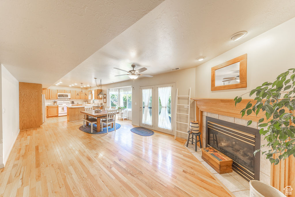 Living room with light wood finished floors, a tiled fireplace, a ceiling fan, recessed lighting, and a textured ceiling