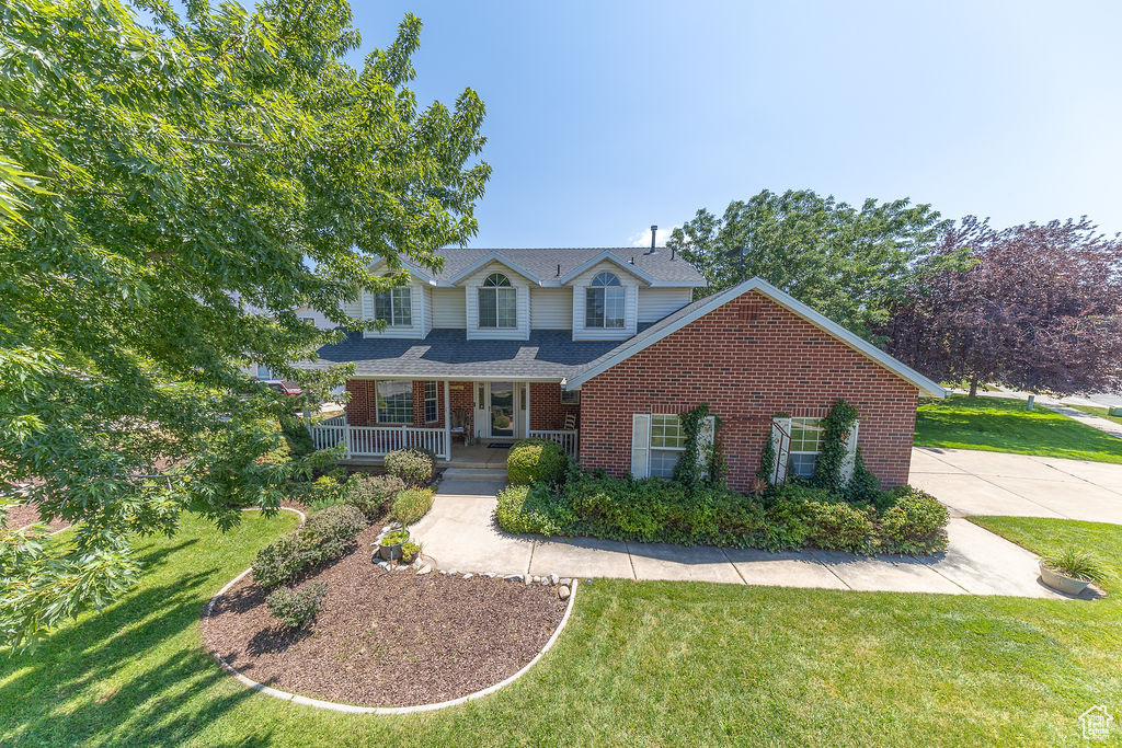 Traditional-style home featuring covered porch, brick siding, a front lawn, and a shingled roof
