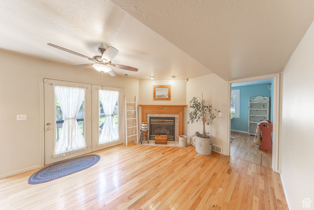 Living room with wood finished floors, ceiling fan, french doors, and a tiled fireplace