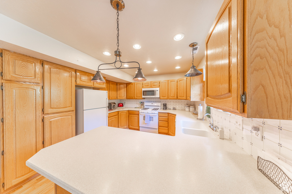 Kitchen featuring white appliances, a peninsula, light countertops, backsplash, and recessed lighting