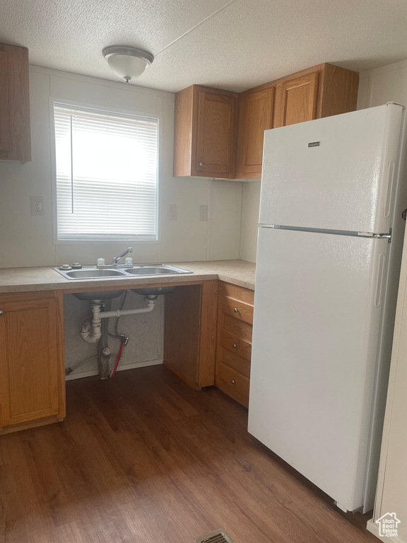 Kitchen featuring freestanding refrigerator, dark wood-type flooring, light countertops, brown cabinetry, and a textured ceiling