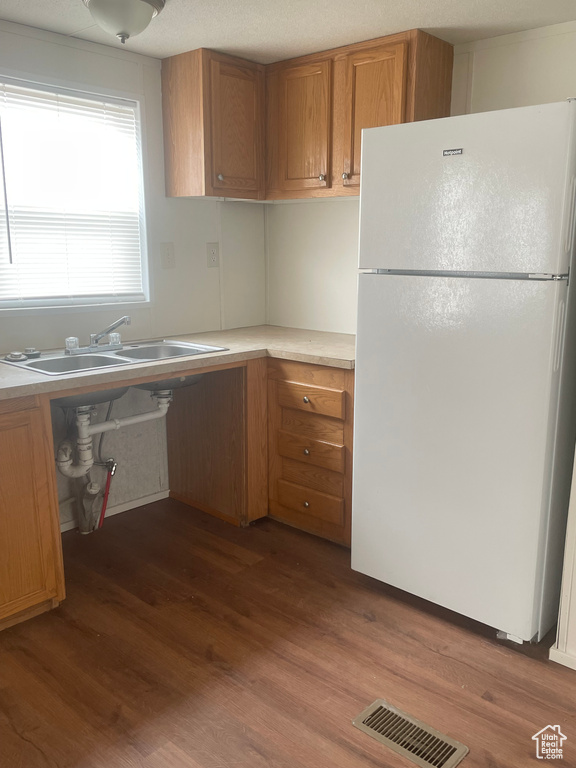 Kitchen with freestanding refrigerator, dark wood-style flooring, and brown cabinets