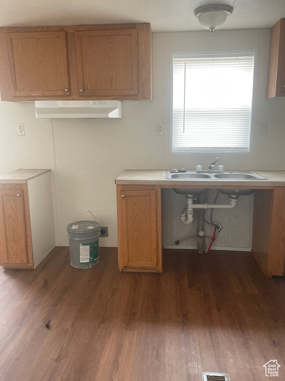 Kitchen featuring dark wood-type flooring, under cabinet range hood, light countertops, and brown cabinets