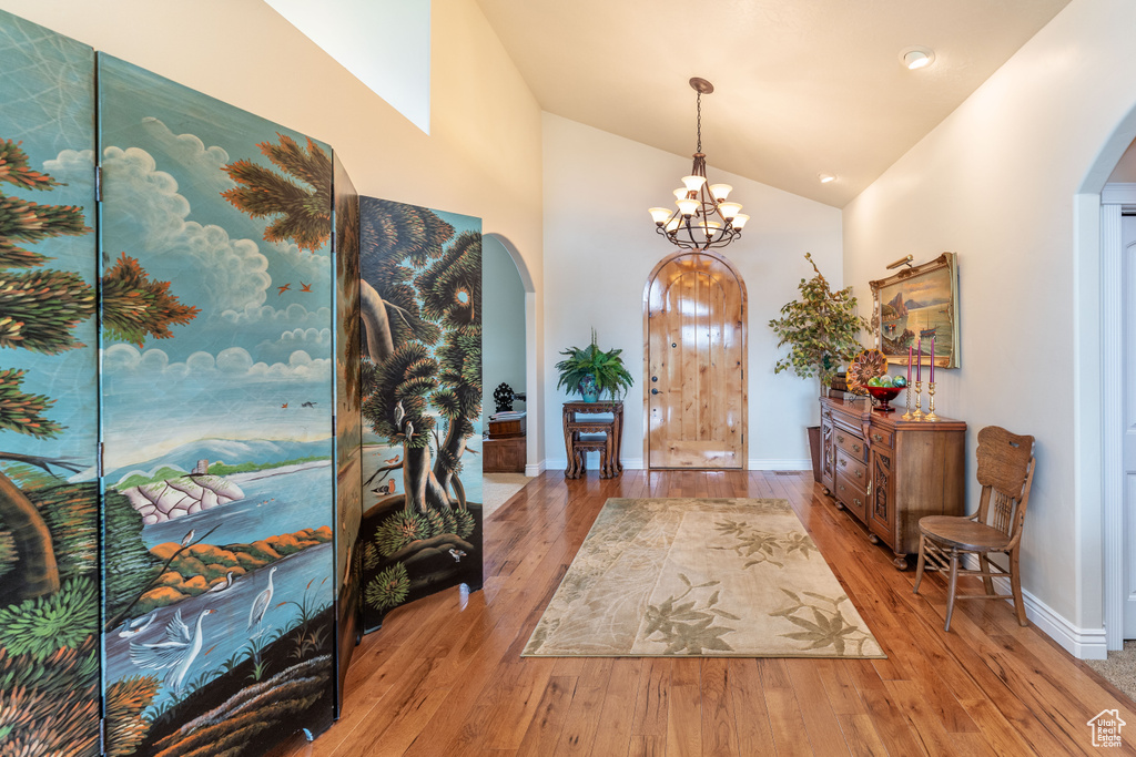 Foyer with arched walkways, wood finished floors, a chandelier, and high vaulted ceiling